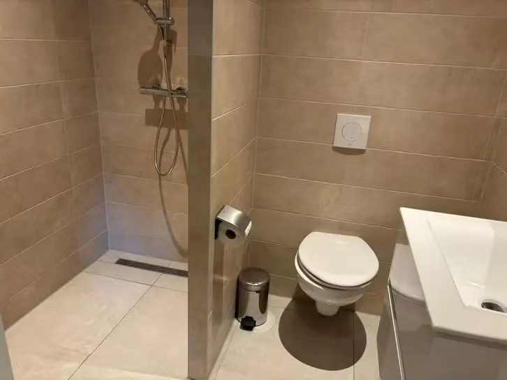 Opgeleverde badkamer met inloopdouche, lijngoot, hangtoilet en beige tegelwerk