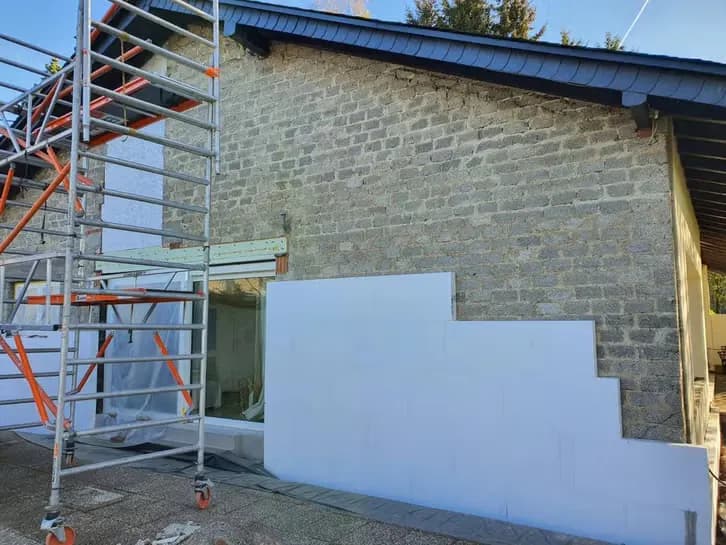 Gable end with white insulation boards being fitted for external wall insulation, scaffold tower in front